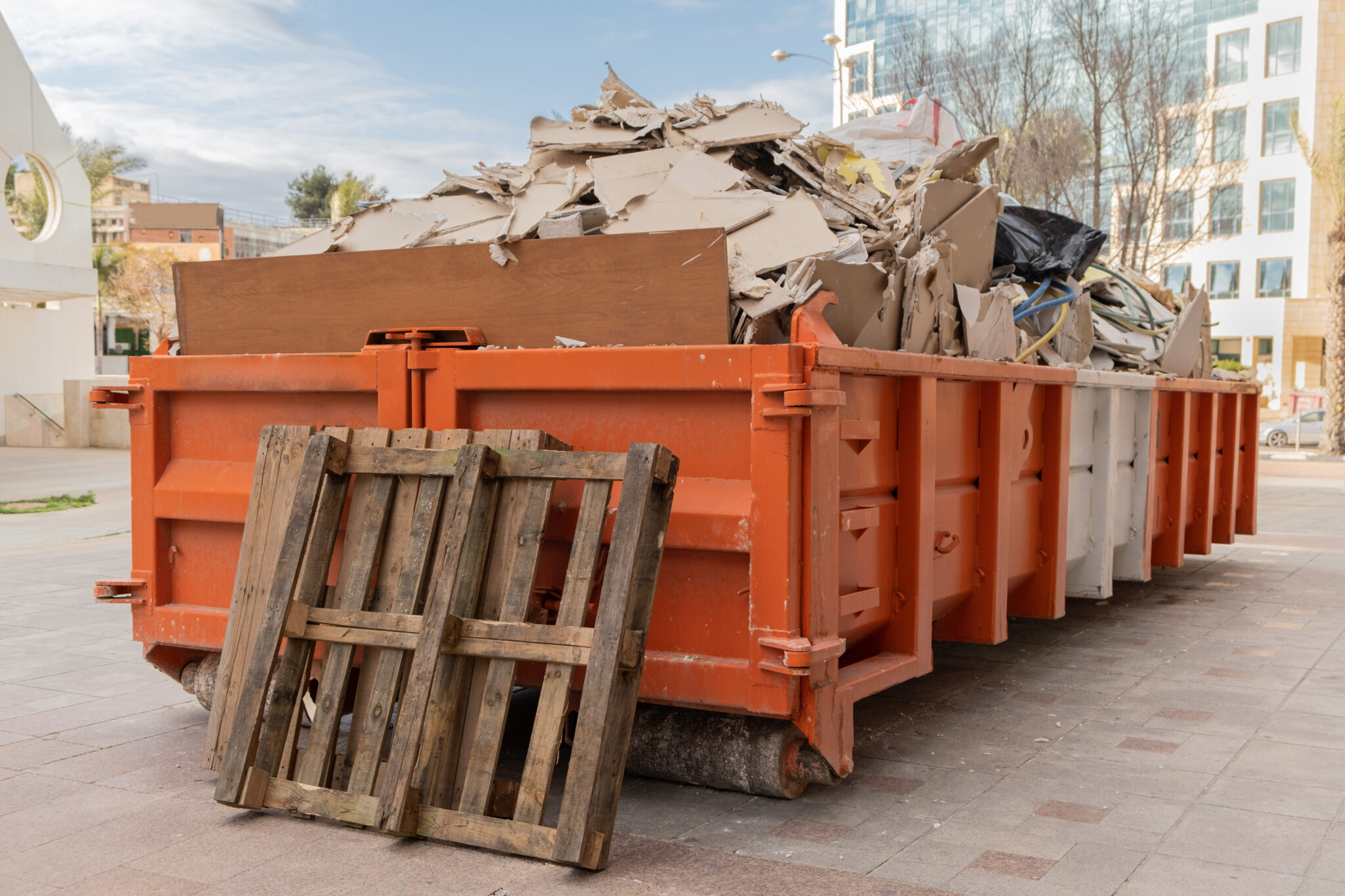 Huge heap on metal Big  Overloaded dumpster waste container filled with construction waste, drywall and other rubble near a construction site.