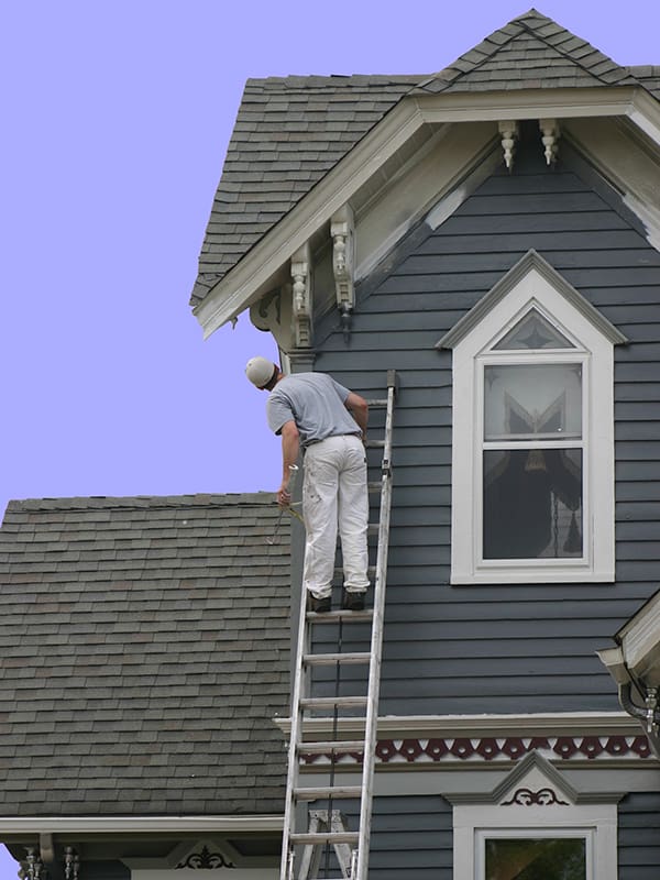 Man on a ladder painting a home's exterior
