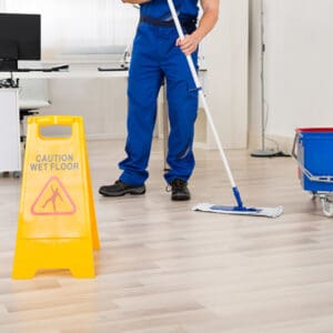 A yellow caution sign with black text that reads 'CAUTION WET FLOOR with a man mopping in the background