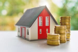 Small model of house next to stacks of gold coins